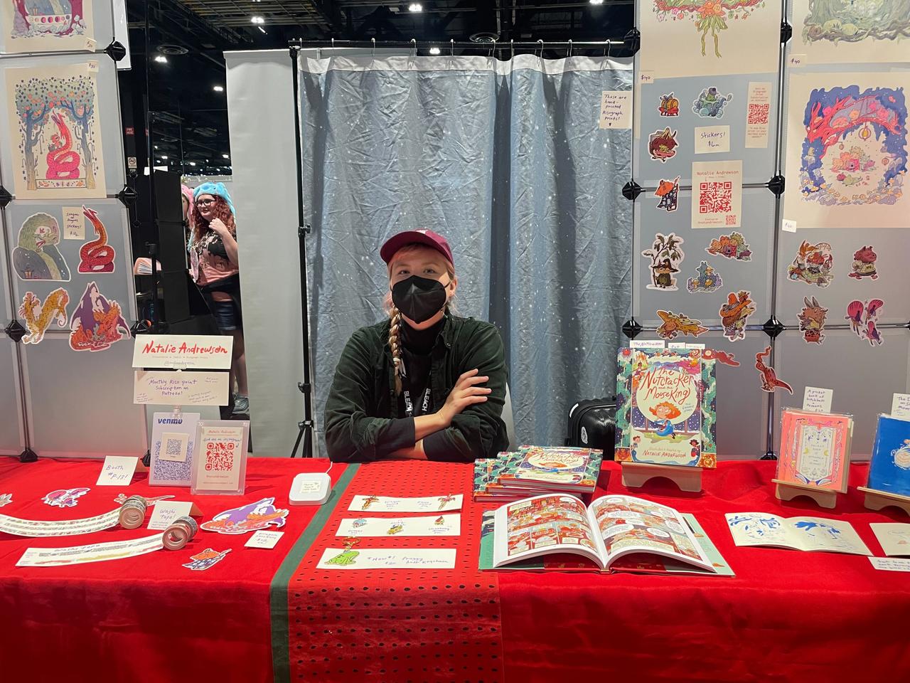 Natalie Anderson behind her table featuring a graphic novel and prints