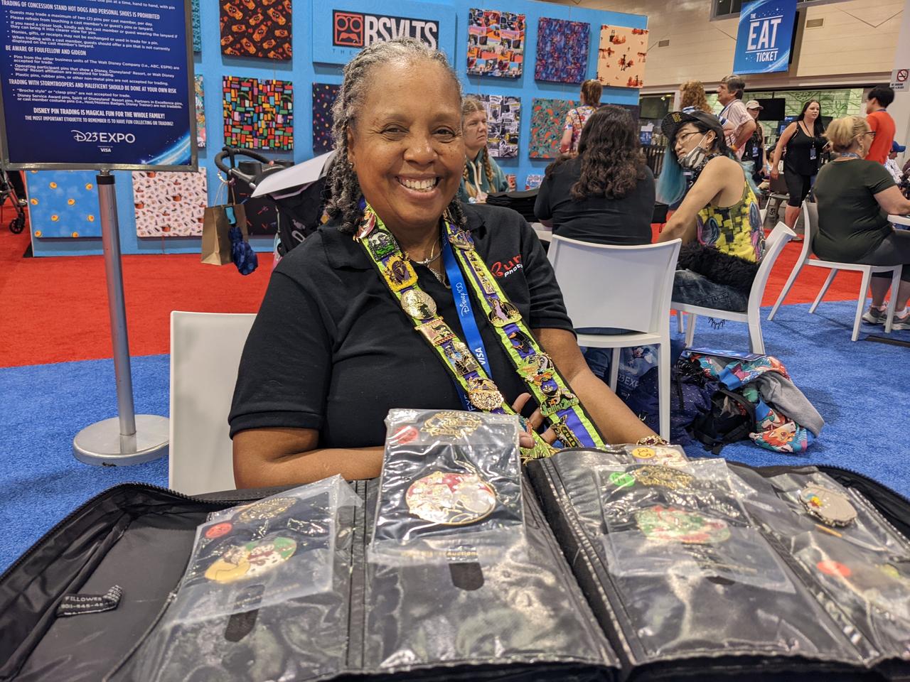 Jeanette Burton smiling, showcasing her book of pins and Maleficent lanyard