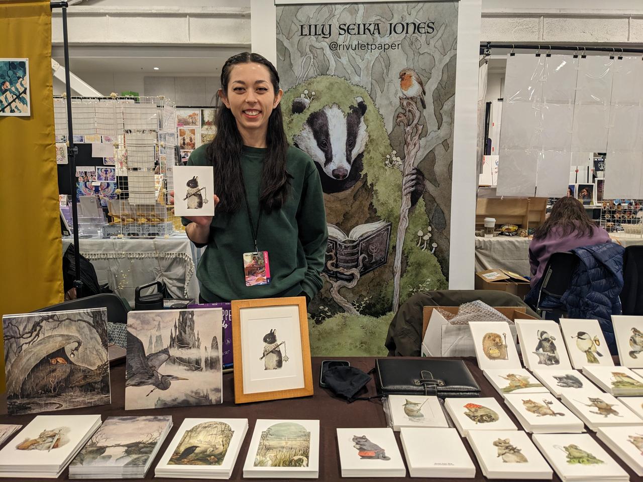 Photograph of artist holding a print behind her table