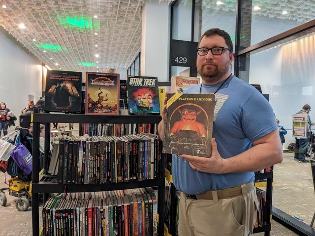 David Carnahan holding a copy of Dungeons and Dragons in front of the library