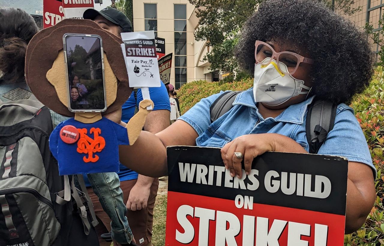 Cadry Ferrer holds a picket sign and a felt puppet of Zayre Ferrer holding an even smaller picket sign