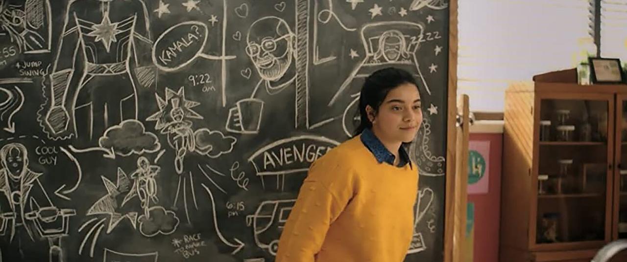 Ms. Marvel still Iman Vellani as Kamala Khan in front of a blackboard filled with superhero based doodles